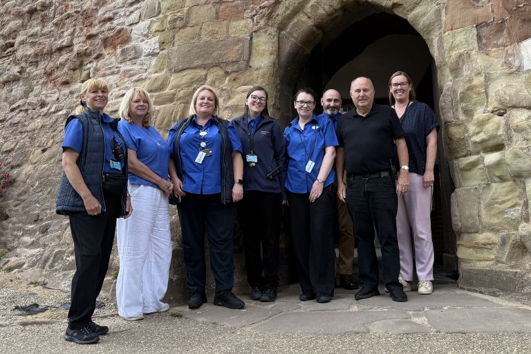 group of people standing outside a brick archway wearing blue top uniform