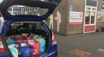 A car with its boot open with lots of bags full of hygiene products parked next to a building