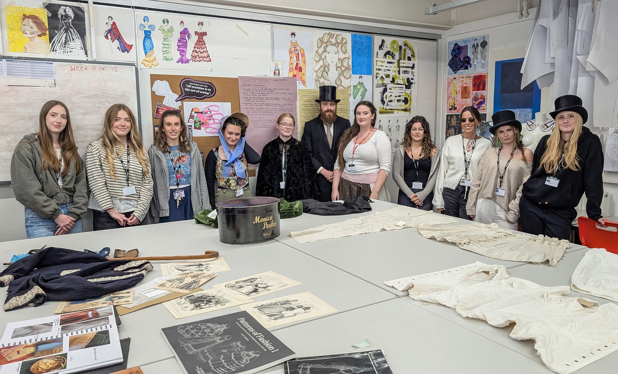 photo of a group of students in a classroom standing by a textiles table 
