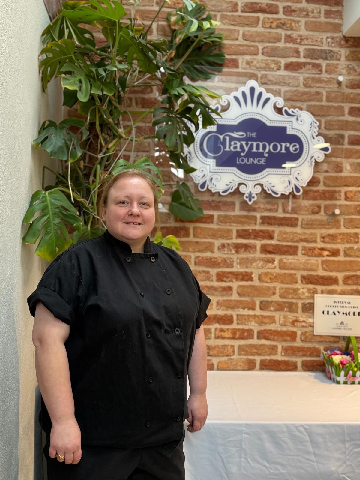 photo of a chef in black jacket standing by a table and brick wall in the claymore lounge