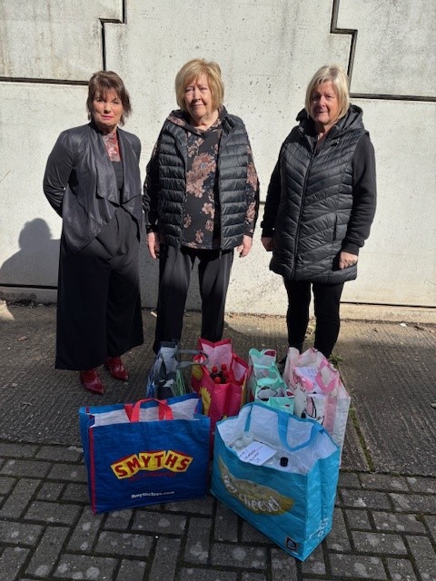 3 ladies standing by bags with hygiene items donated