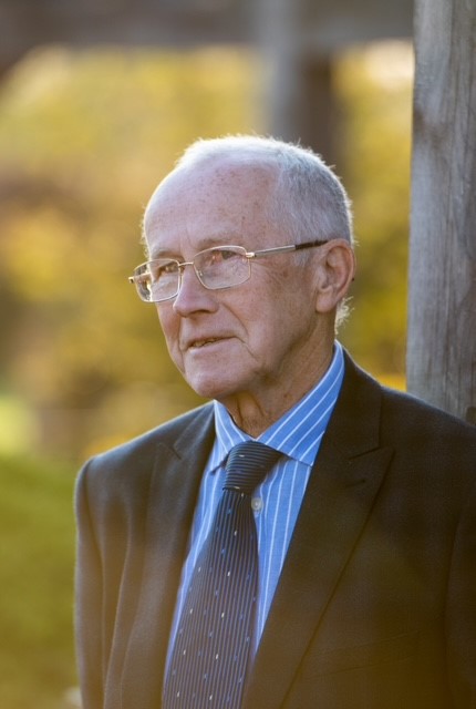 photo of a man with grey hair, glasses and wearing a blue shirt, tie and dark jacket