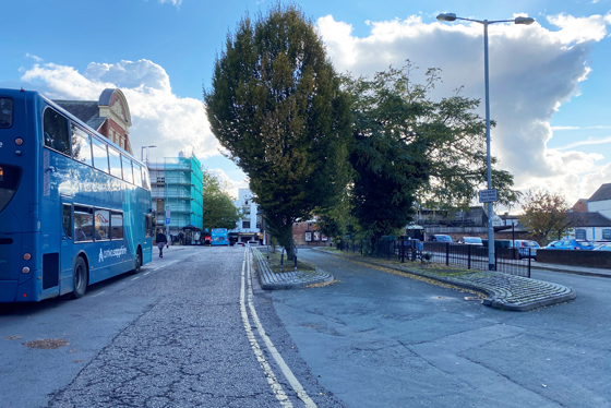 A road with a bus parked on the left. Trees in the middle and a car park on the right