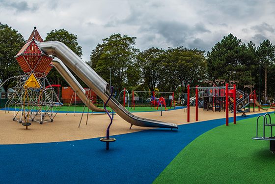 Castle play area with play equipment like slides, swings and frames. The floor is blue, green and beige