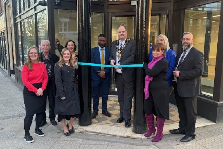 group photo outside a building with dark pillows, teal ribbon being cut