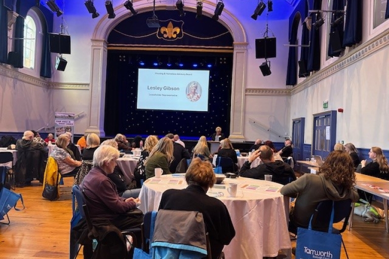 image of a room with a stage and screen and people sitting at round tables