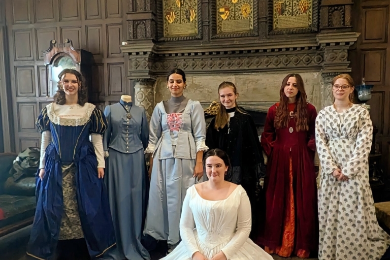people sitting and standing in Victorian clothes by a fireplace and wooden panel walls