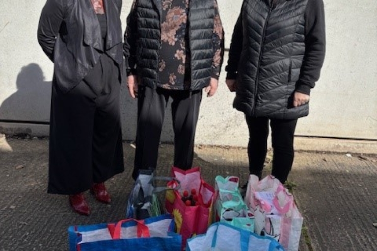 3 ladies standing by bags with hygiene items donated