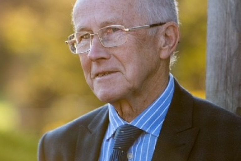 photo of a man with grey hair, glasses and wearing a blue shirt, tie and dark jacket