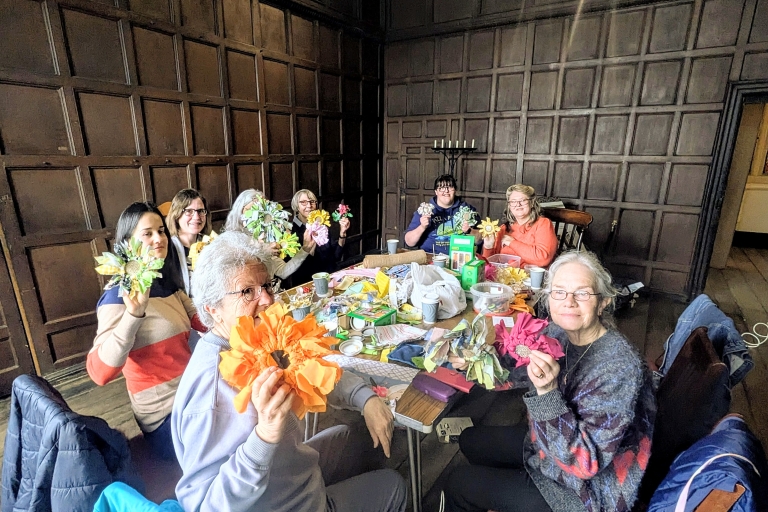 photo of a group of people in a room with dark wooden panelling, holding handmade material and wool flowers