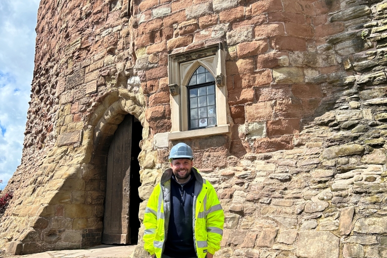 photo of a person wearing a hi vis jacket, hard hat outside the front of a castle building
