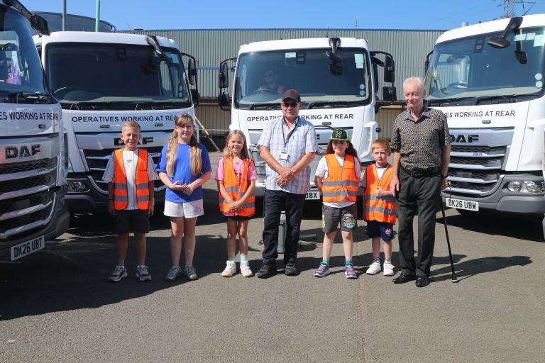 children standing by 3 white food waste trucks