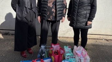 3 ladies standing by bags with hygiene items donated