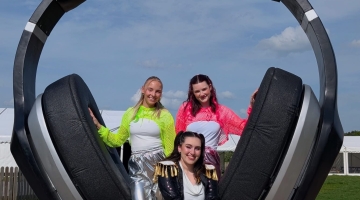 image of large headphones with 3 females wearing a yellow, pink and dark jacket 
