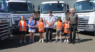 children standing by 3 white food waste trucks